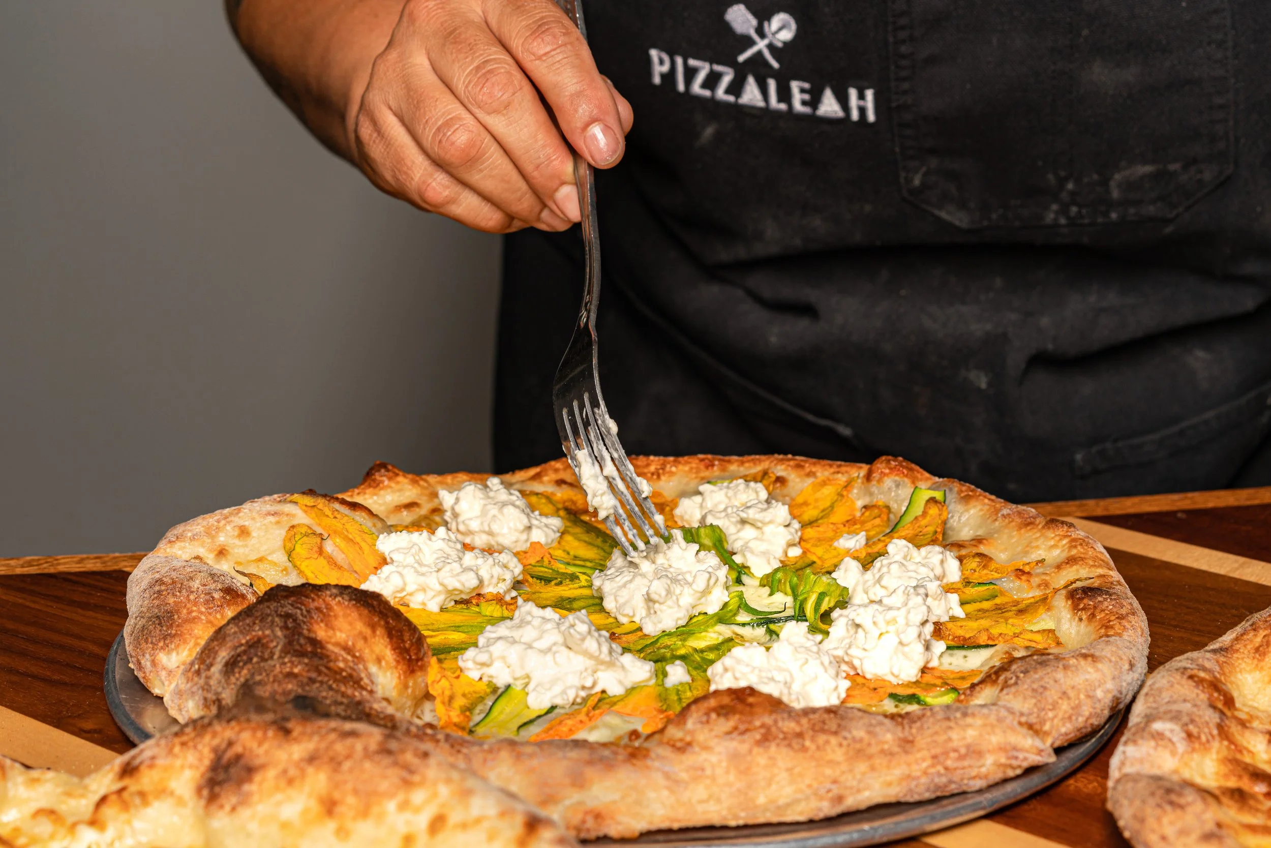 Chef adding ricotta to zucchini blossom pizza